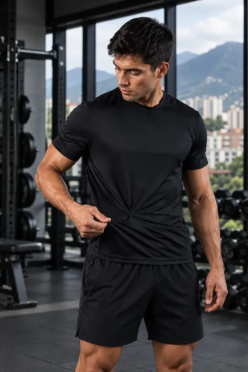 Hombre mostrando la elasticidad de una camiseta deportiva negra de At Fit Sport en el gimnasio.